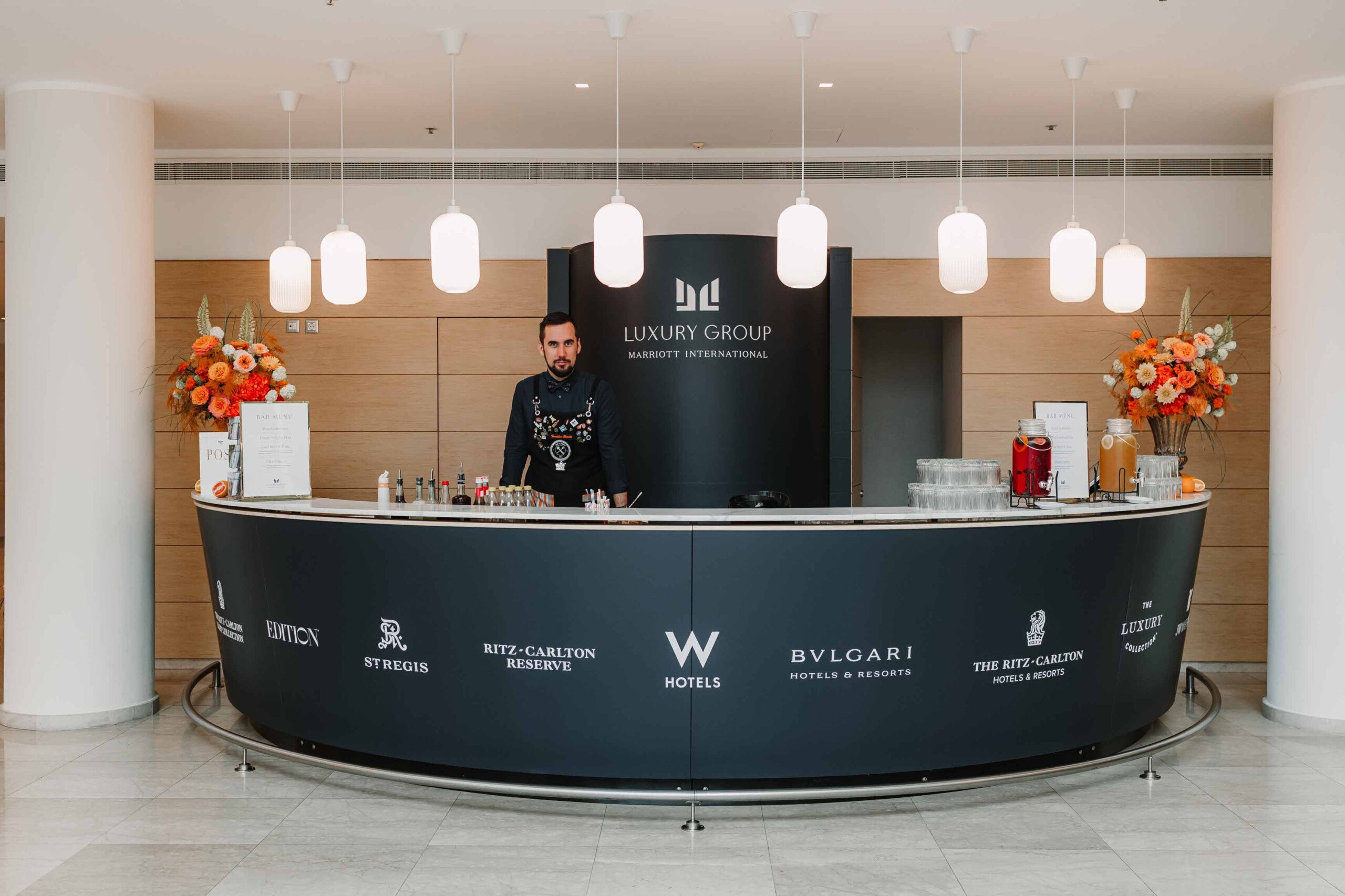 Bartender at a custom-branded curved bar featuring Marriott Luxury Group hotel logos