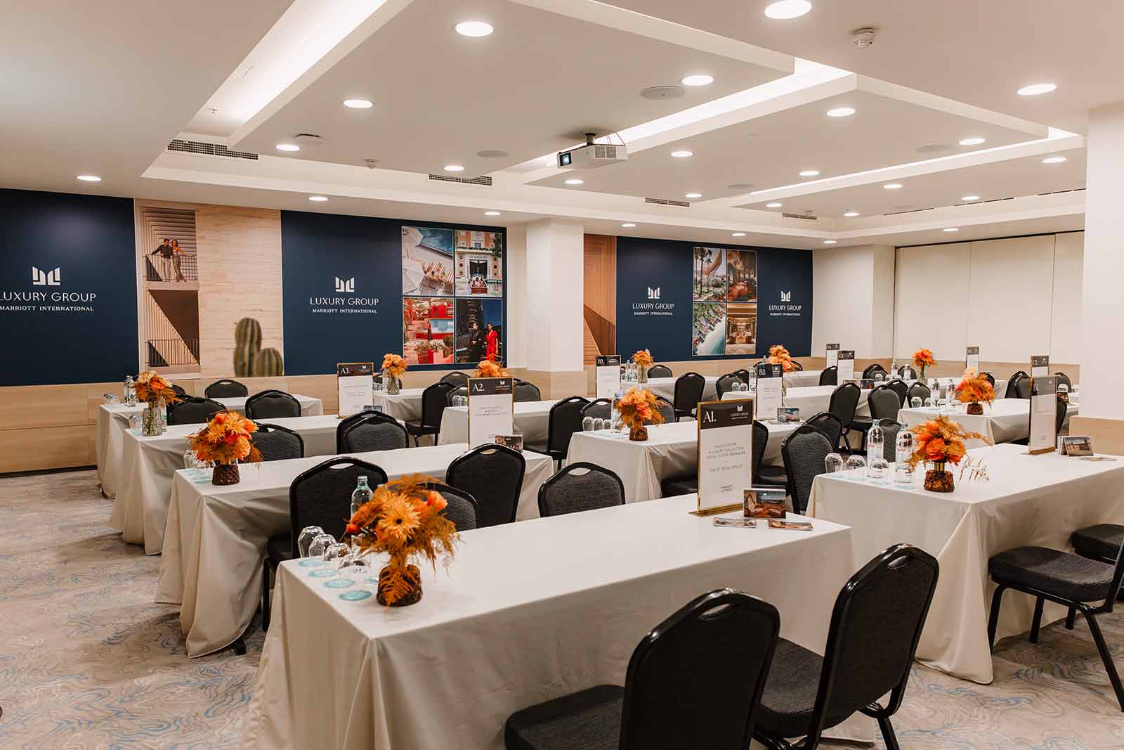 Conference room set with classroom seating and large branded wall panels showing Marriott Luxury Group destinations