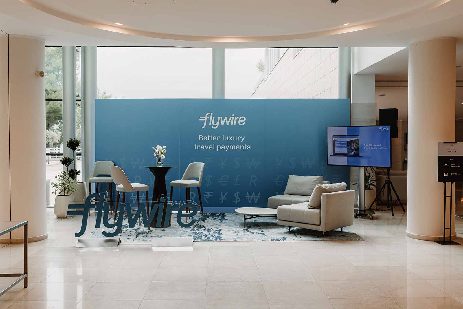 Branded Flywire event lounge with blue backdrop wall and 3D logo at Hotel Lav