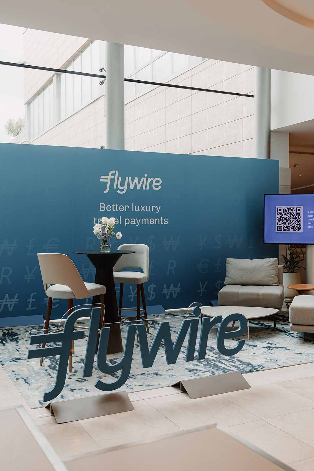Freestanding Flywire 3D acrylic logo in front of a blue branded wall and lounge seating